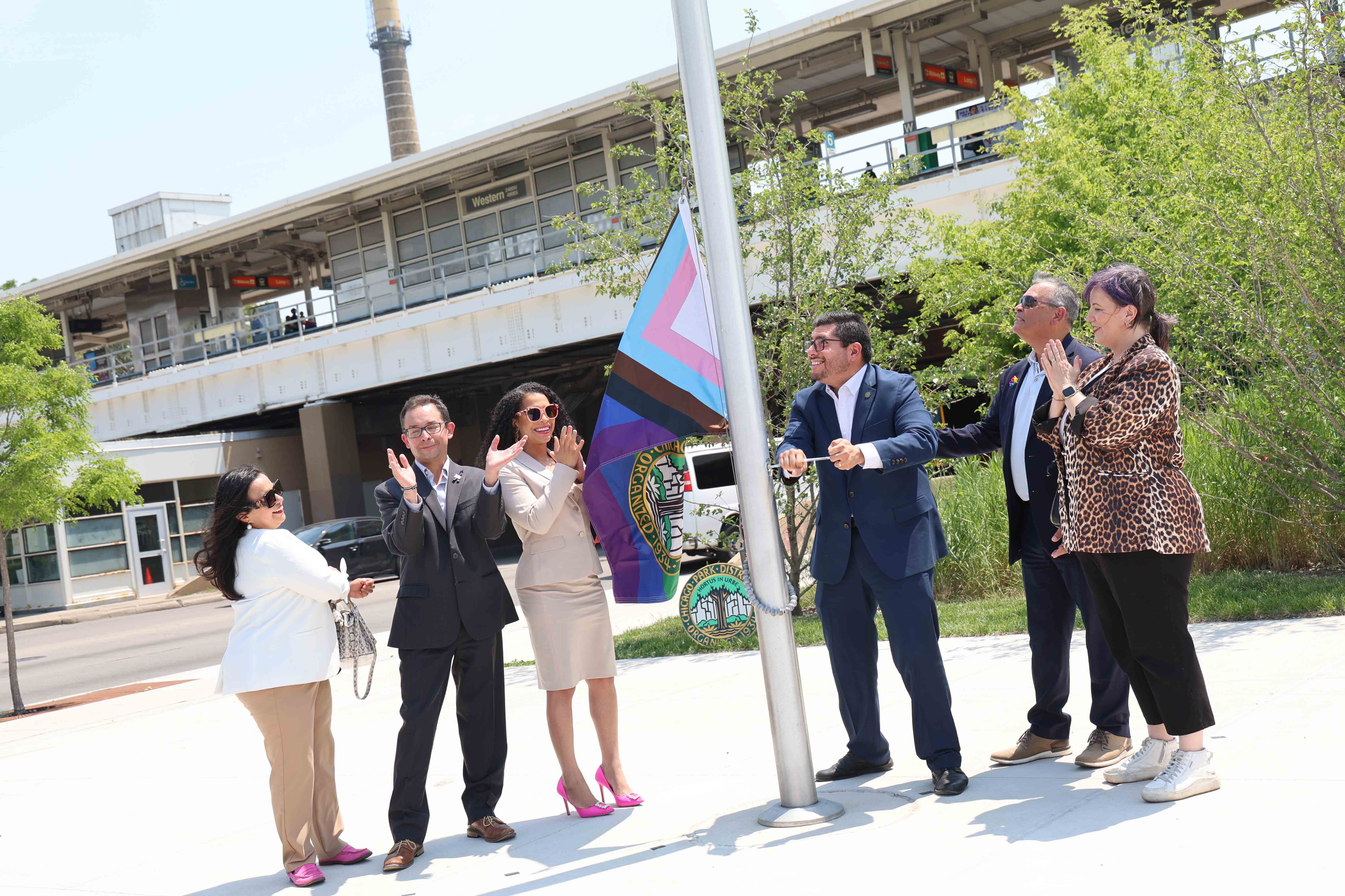 Group raising Progress Pride flag at a ceremony.